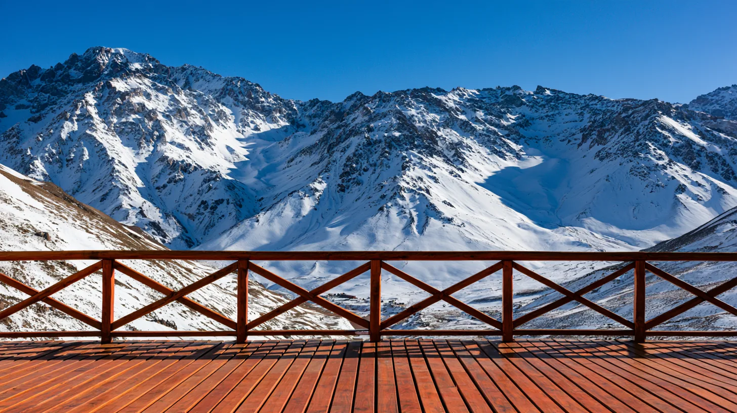 Scenic view of snow-covered mountains under a clear blue sky, with a wooden railing in the foreground.